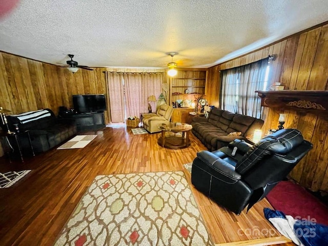 living room featuring a textured ceiling, hardwood / wood-style flooring, ceiling fan, and wooden walls