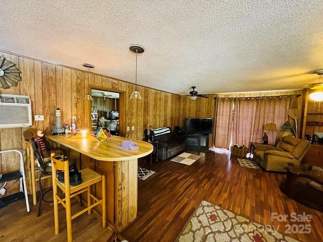 kitchen with ceiling fan, dark wood-type flooring, a wall unit AC, kitchen peninsula, and a breakfast bar area