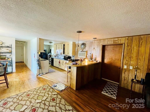 kitchen featuring kitchen peninsula, light wood-type flooring, a textured ceiling, wooden walls, and pendant lighting