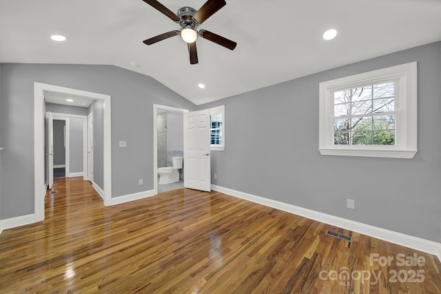 unfurnished bedroom with ceiling fan, ensuite bathroom, vaulted ceiling, and hardwood / wood-style floors