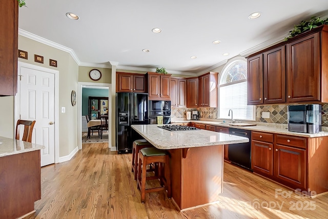 kitchen featuring black appliances, light wood-type flooring, crown molding, light stone counters, and a kitchen island