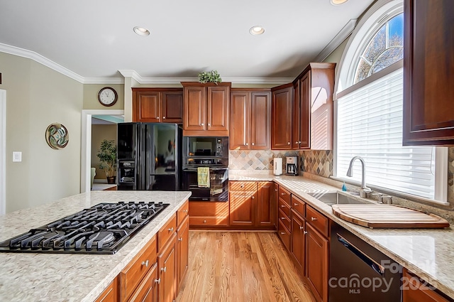 kitchen featuring sink, light stone counters, light wood-type flooring, ornamental molding, and black appliances