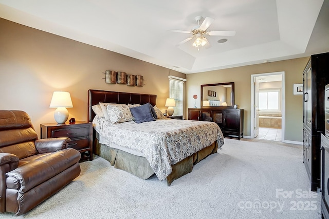 bedroom featuring connected bathroom, light carpet, ceiling fan, and a tray ceiling