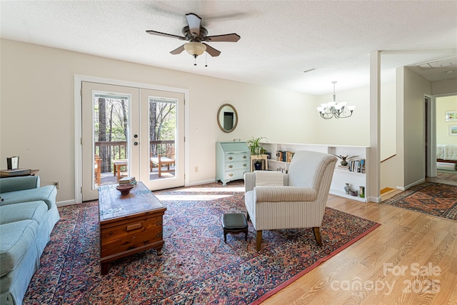 living room with ceiling fan with notable chandelier, a textured ceiling, french doors, and light wood-type flooring