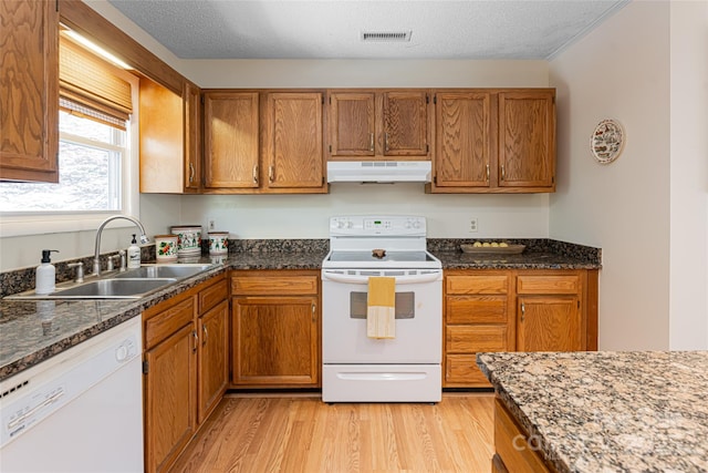 kitchen featuring white appliances, a textured ceiling, dark stone counters, light hardwood / wood-style floors, and sink