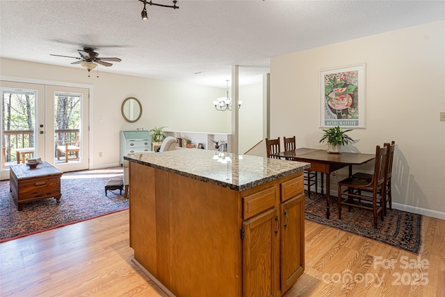 kitchen with french doors, a textured ceiling, a kitchen island, ceiling fan with notable chandelier, and light hardwood / wood-style flooring