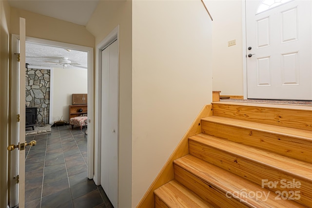 staircase featuring a textured ceiling, ceiling fan, and a wood stove