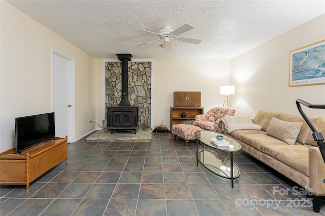 living room featuring ceiling fan, a wood stove, and a textured ceiling