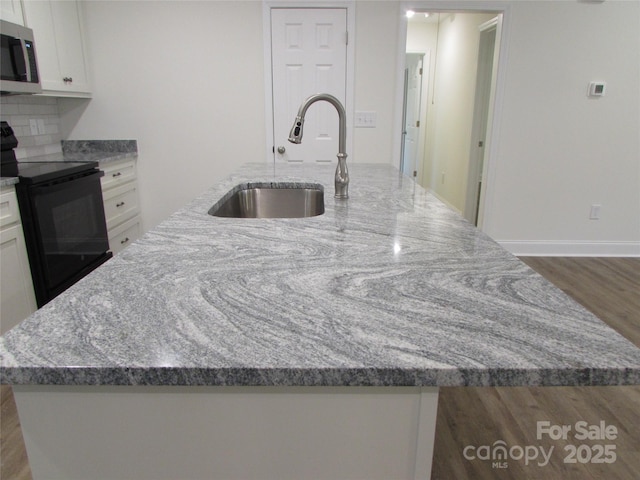 kitchen with light stone countertops, sink, black / electric stove, an island with sink, and white cabinets