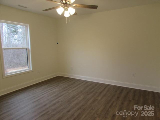 empty room with a wealth of natural light, dark wood-type flooring, and ceiling fan