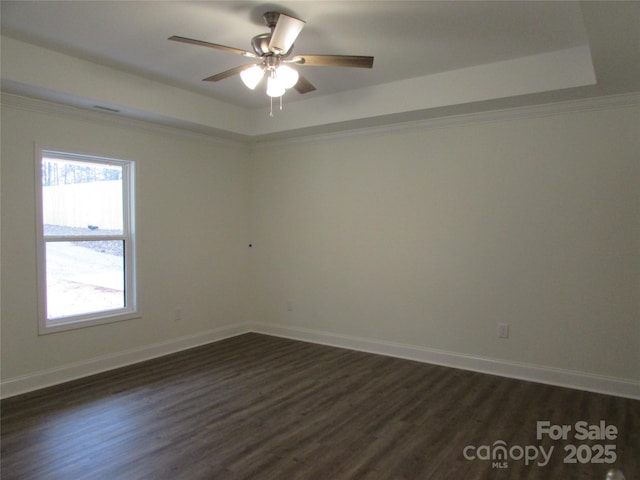 empty room featuring a tray ceiling, ceiling fan, dark wood-type flooring, and ornamental molding