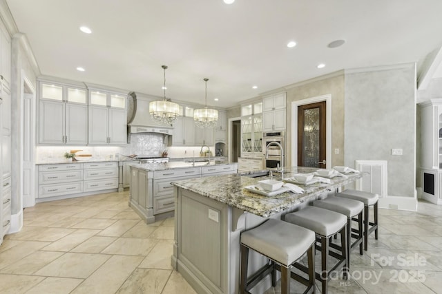 kitchen with backsplash, premium range hood, a spacious island, hanging light fixtures, and light stone counters