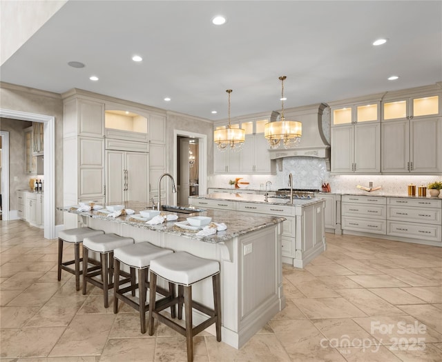 kitchen featuring light stone countertops, sink, hanging light fixtures, paneled fridge, and a large island with sink