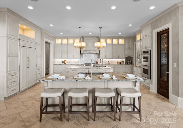 kitchen with double oven, light stone countertops, pendant lighting, and a spacious island