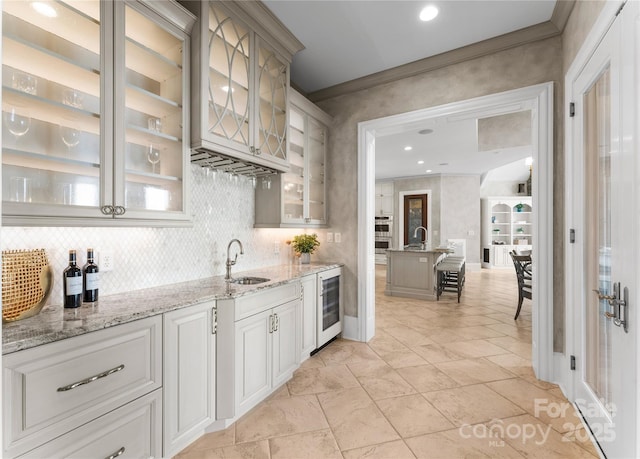 bar with white cabinets, sink, wine cooler, decorative backsplash, and light stone countertops