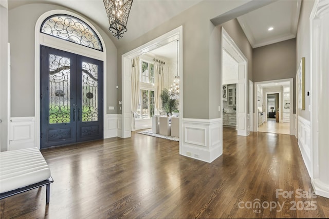 foyer entrance featuring a notable chandelier, dark hardwood / wood-style flooring, crown molding, and french doors