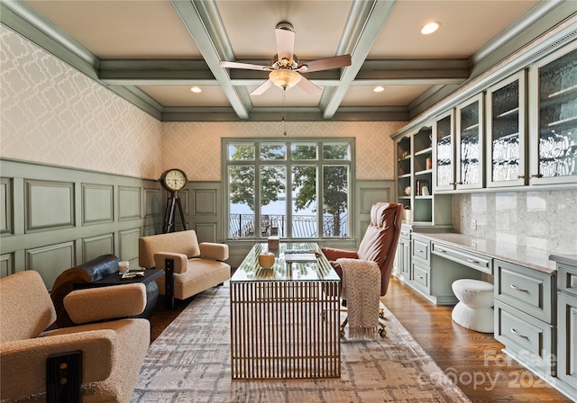 interior space with coffered ceiling, ceiling fan, built in desk, beamed ceiling, and dark hardwood / wood-style flooring