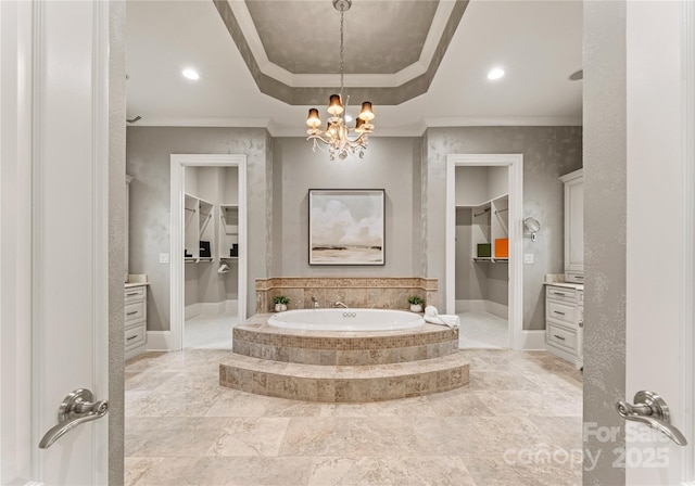 bathroom featuring vanity, a raised ceiling, crown molding, a relaxing tiled tub, and a notable chandelier