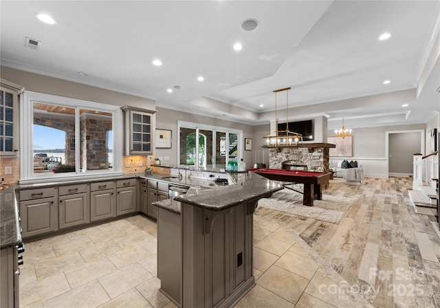 kitchen with a kitchen bar, gray cabinetry, a raised ceiling, dark stone countertops, and hanging light fixtures