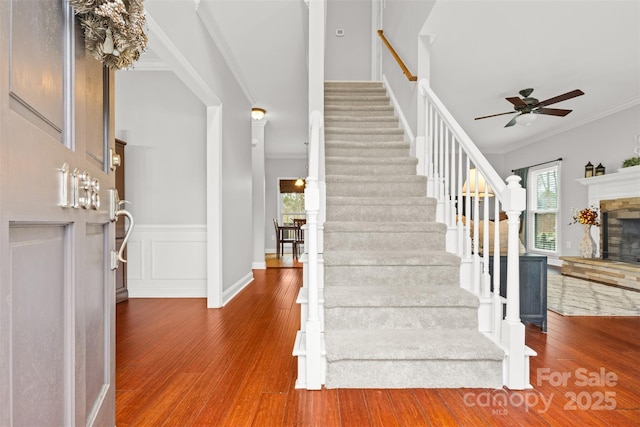 stairway with a healthy amount of sunlight, ceiling fan, ornamental molding, and hardwood / wood-style floors