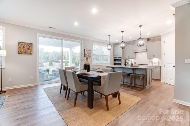 dining space featuring ornamental molding, sink, and light hardwood / wood-style flooring