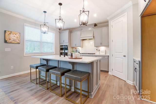 kitchen featuring crown molding, a kitchen bar, a kitchen island with sink, and hanging light fixtures