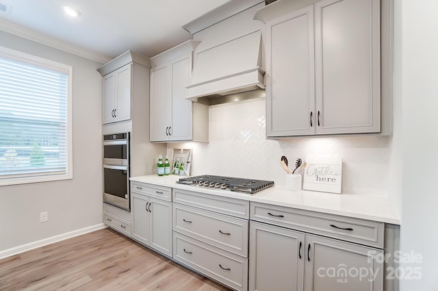 kitchen featuring appliances with stainless steel finishes, decorative backsplash, ornamental molding, custom range hood, and light hardwood / wood-style flooring