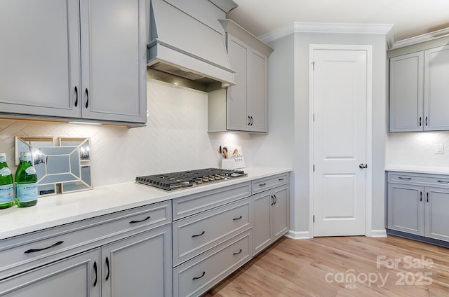 kitchen with premium range hood, gray cabinetry, light hardwood / wood-style floors, ornamental molding, and stainless steel gas cooktop