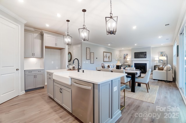 kitchen with gray cabinets, dishwasher, an island with sink, hanging light fixtures, and light wood-type flooring