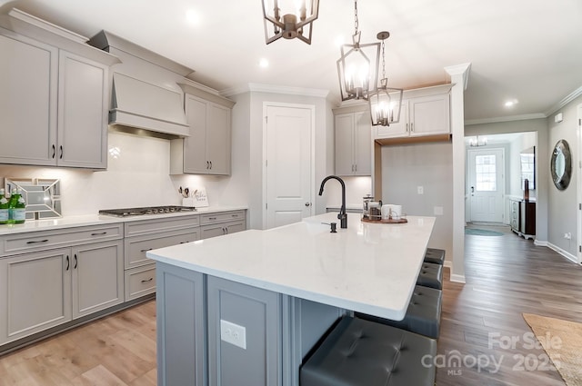 kitchen featuring hanging light fixtures, a center island with sink, gray cabinets, custom range hood, and stainless steel gas stovetop