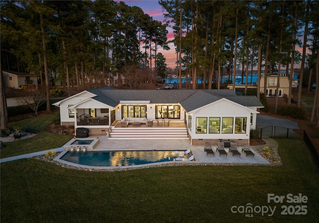 back house at dusk featuring a lawn, an outdoor living space, a swimming pool with hot tub, and a patio area