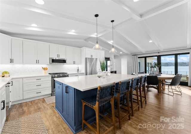 kitchen with appliances with stainless steel finishes, pendant lighting, a water view, a center island, and white cabinetry