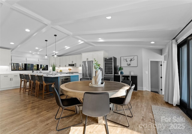 dining room with vaulted ceiling with beams and light hardwood / wood-style flooring