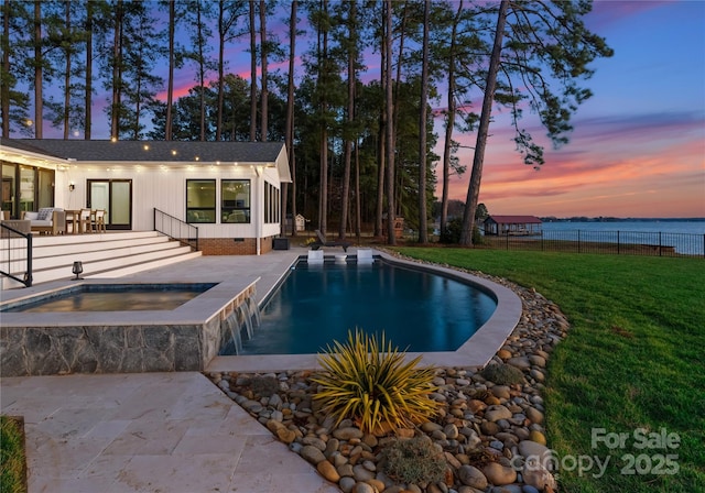 pool at dusk featuring a lawn, an in ground hot tub, a water view, and a patio