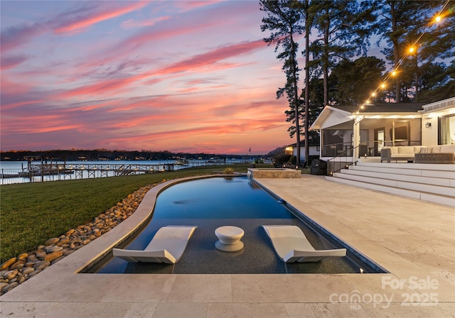 pool at dusk with a sunroom, a water view, a yard, and a patio