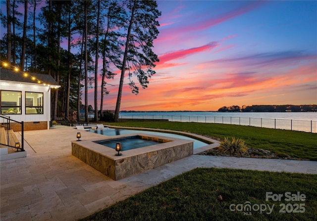 pool at dusk with an in ground hot tub, a yard, a water view, and a patio