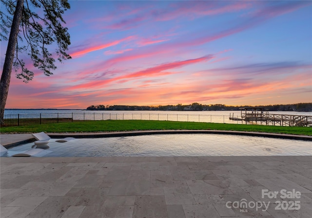 pool at dusk featuring a lawn and a water view