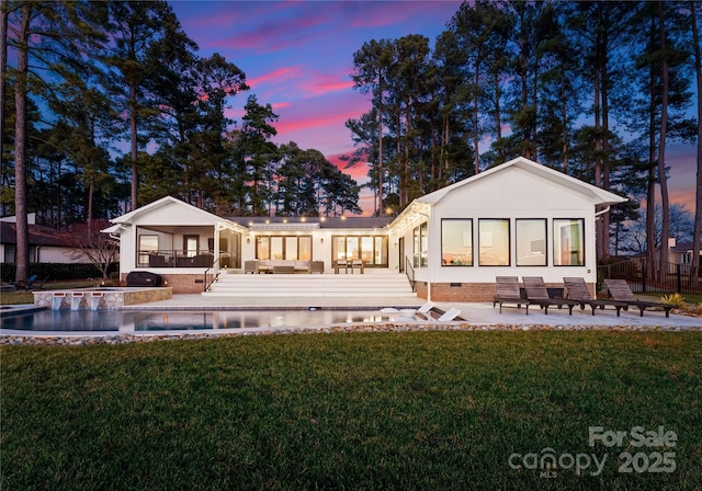 back house at dusk with a sunroom, a pool side deck, a yard, and a patio