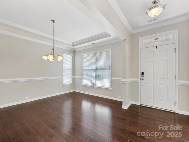 foyer with a notable chandelier, dark hardwood / wood-style floors, a raised ceiling, and ornamental molding