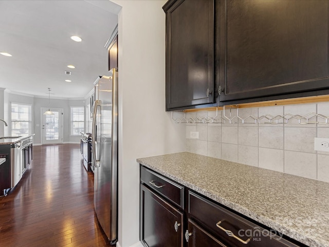 kitchen featuring decorative backsplash, stainless steel fridge, light stone counters, ornamental molding, and decorative light fixtures