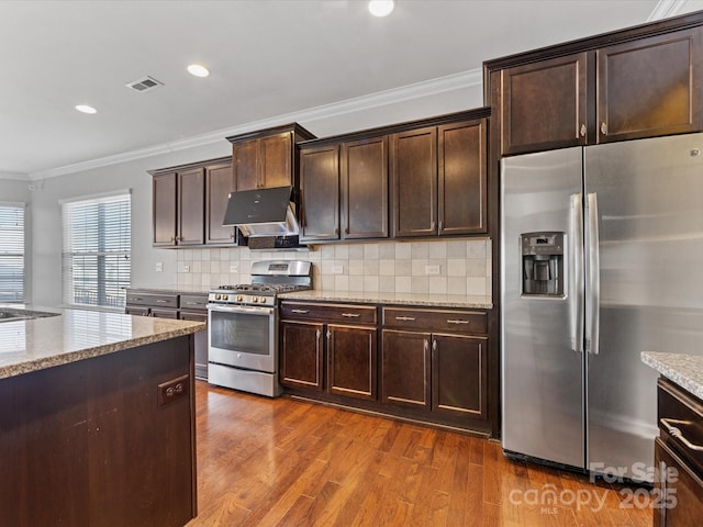 kitchen with decorative backsplash, light stone countertops, ornamental molding, appliances with stainless steel finishes, and dark brown cabinets