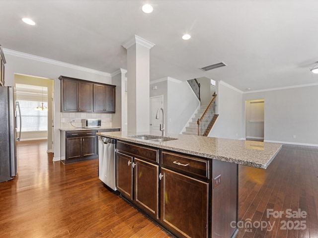 kitchen featuring a kitchen island with sink, sink, dark brown cabinets, light stone counters, and stainless steel appliances