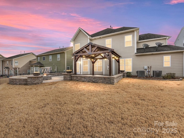 back house at dusk featuring a gazebo, a fire pit, central air condition unit, and a lawn