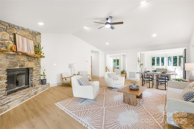 living room featuring ceiling fan, a stone fireplace, light wood-type flooring, and lofted ceiling