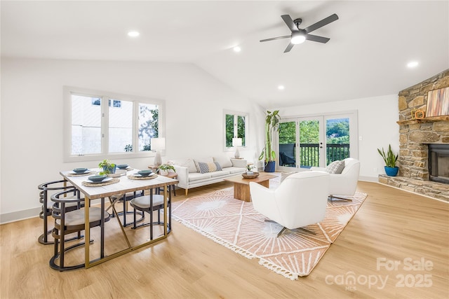 living room with a fireplace, light wood-type flooring, vaulted ceiling, and ceiling fan