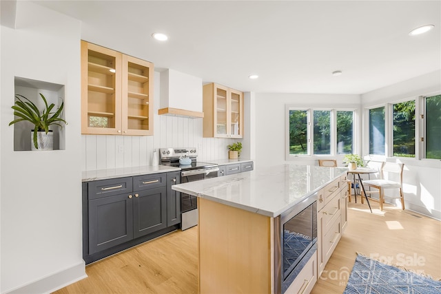 kitchen with a center island, light hardwood / wood-style flooring, light stone countertops, custom range hood, and stainless steel appliances