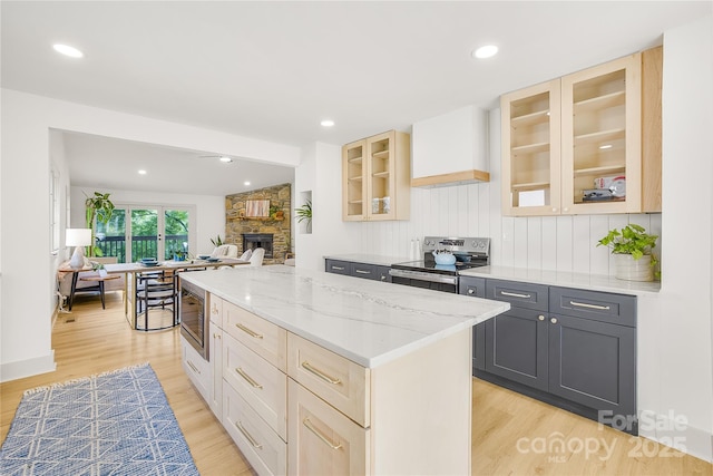 kitchen with gray cabinetry, a center island, a fireplace, light stone counters, and stainless steel appliances