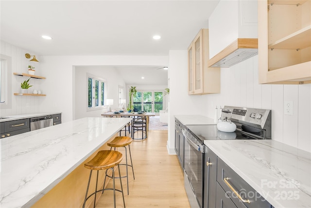 kitchen with light stone countertops, wall chimney exhaust hood, light hardwood / wood-style flooring, a breakfast bar, and appliances with stainless steel finishes