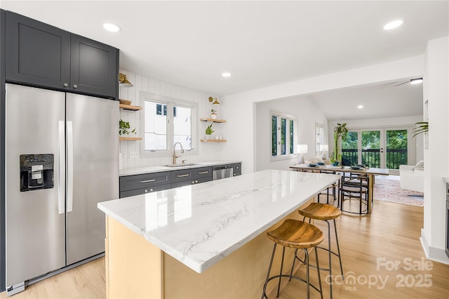 kitchen featuring a kitchen breakfast bar, light stone counters, stainless steel appliances, sink, and a center island