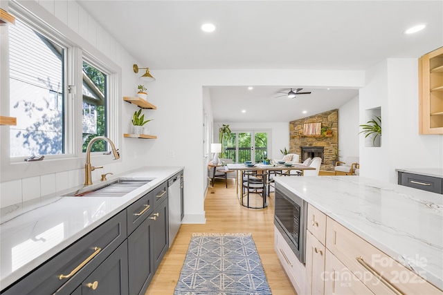 kitchen with built in microwave, sink, ceiling fan, a stone fireplace, and light stone counters